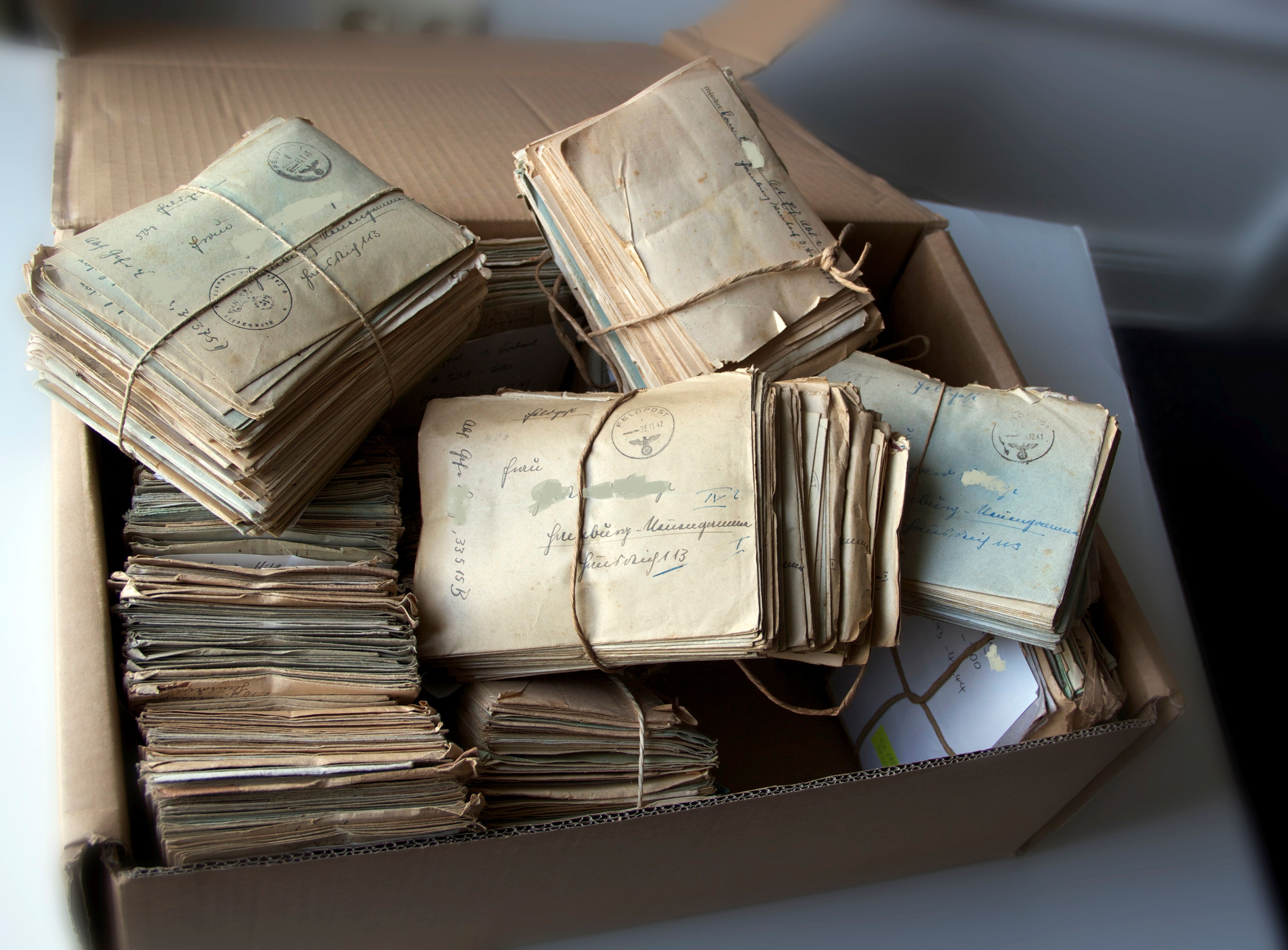 Abbildung mehrerer Bündel Briefe aus dem Konvolut Neuengamme, von Kordeln zusammengehalten, in einem Schuhkarton durcheinander gewürfelt. 