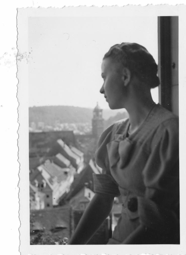 Hilde Nordhoff im Profil, aus einer Höhe auf eine Stadt schauend. Im Hintergrund ein Turm. 