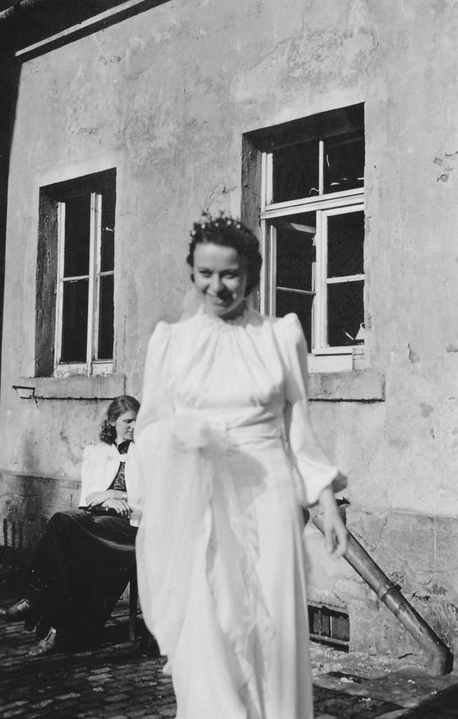 Hilde Nordhoff lächelt in die Kamera, im weißen Hochzeitskleid vor einem Gebäude stehend. 