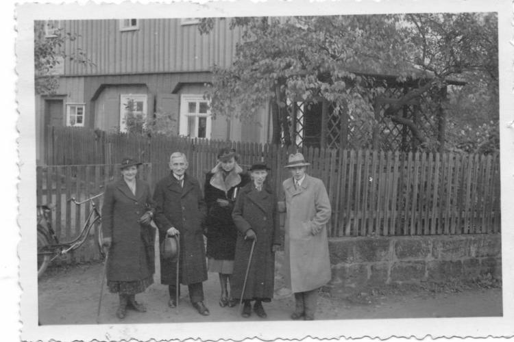 Hilde und Roland Nordhoff stehen mit drei weiteren Personen vor einem Wohnhaus am Gartenzaun an einer Straße. 