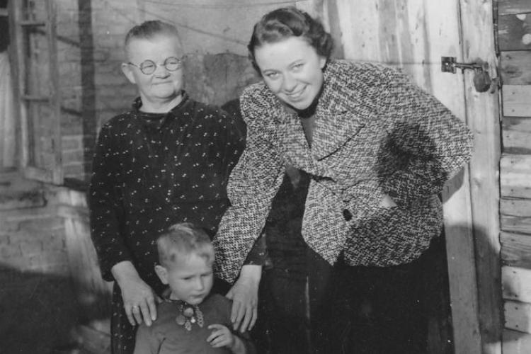 Hilde Nordhoff steht neben einer älteren Frau vor einer Hauswand und beugt sich zu einem Kind herunter. Der Schatten des Fotografen Roland Nordhoff ist ebenfalls zu sehen.