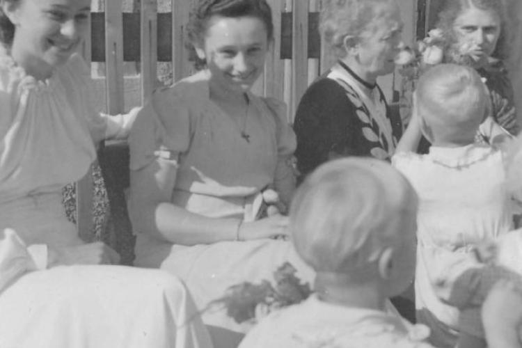 Hilde Nordhoff sitzt mit Hochzeitsgästen vor einem Gartenzaun.