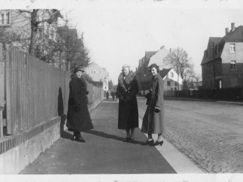 Drei Personen stehen auf einem Bürgersteig in einer Kleinstadt. Eine davon ist Hilde Nordhoff.