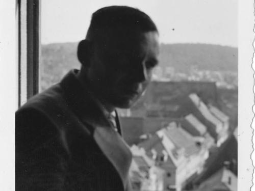 Nahaufnahme von Roland Nordhoff, in einem Fensterrahmen sitzend. Im Hintergrund die Dächer einer Stadt und in der Ferne Berge. 