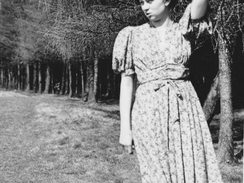 Hilde Nordhoff posiert vor einem Baum für die Kamera. Ihr Blick geht zur Seite weg in die Ferne, ihre Hand lehnt am Hinterkopf.