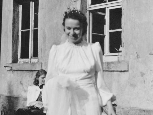 Hilde Nordhoff lächelt in die Kamera, im weißen Hochzeitskleid vor einem Gebäude stehend. 