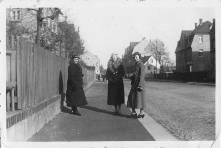 Drei Personen stehen auf einem Bürgersteig in einer Kleinstadt. Eine davon ist Hilde Nordhoff.