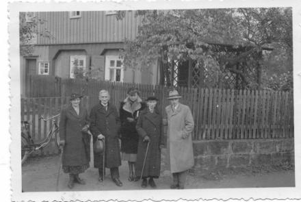 Hilde und Roland Nordhoff stehen mit drei weiteren Personen vor einem Wohnhaus am Gartenzaun an einer Straße. 