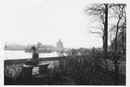 Hilde Nordhoff sitzt auf einer Bank mit Blick auf den Hafen von Eckernförde. Im Hintergrund ist ein markantes Backsteingebäude zu sehen. Das ist der Rundspeicher am Hafen von Eckernförde.